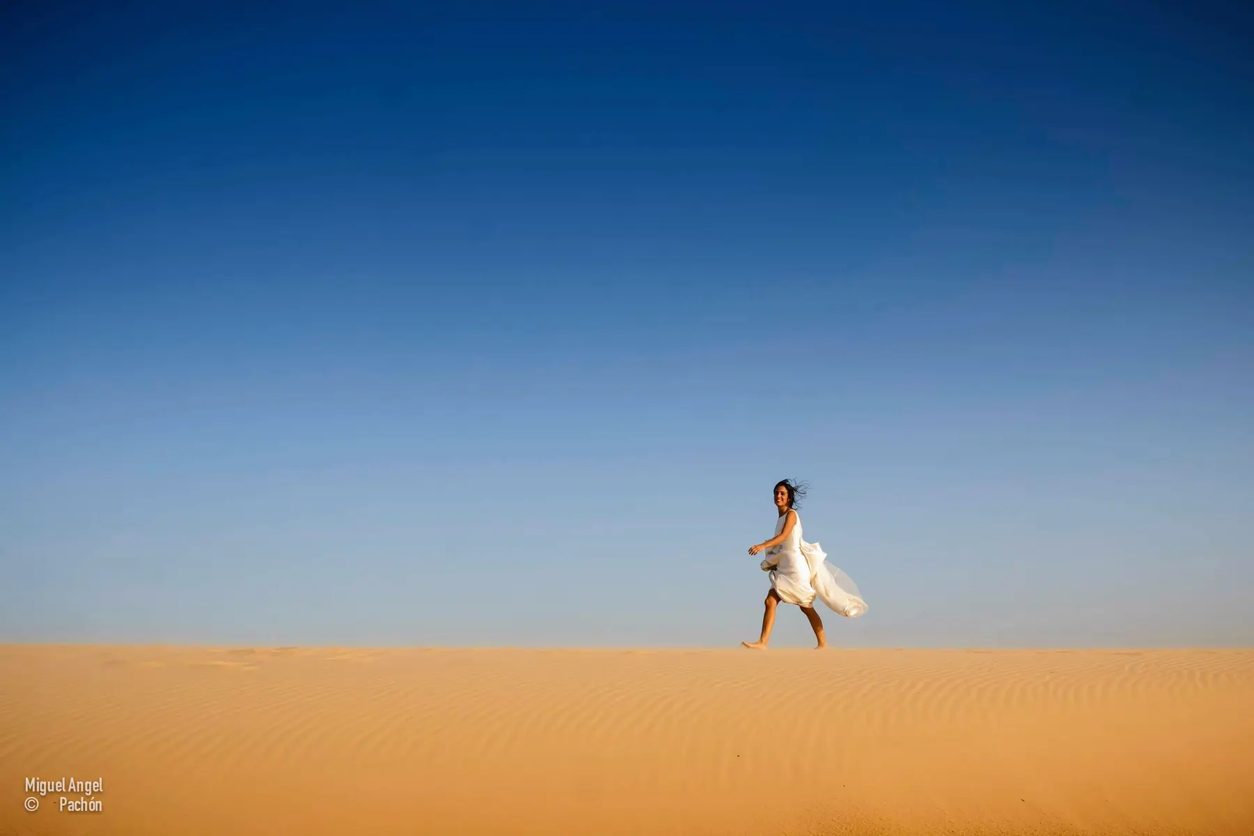 Novia caminando sobre una duna bajo el cielo azul