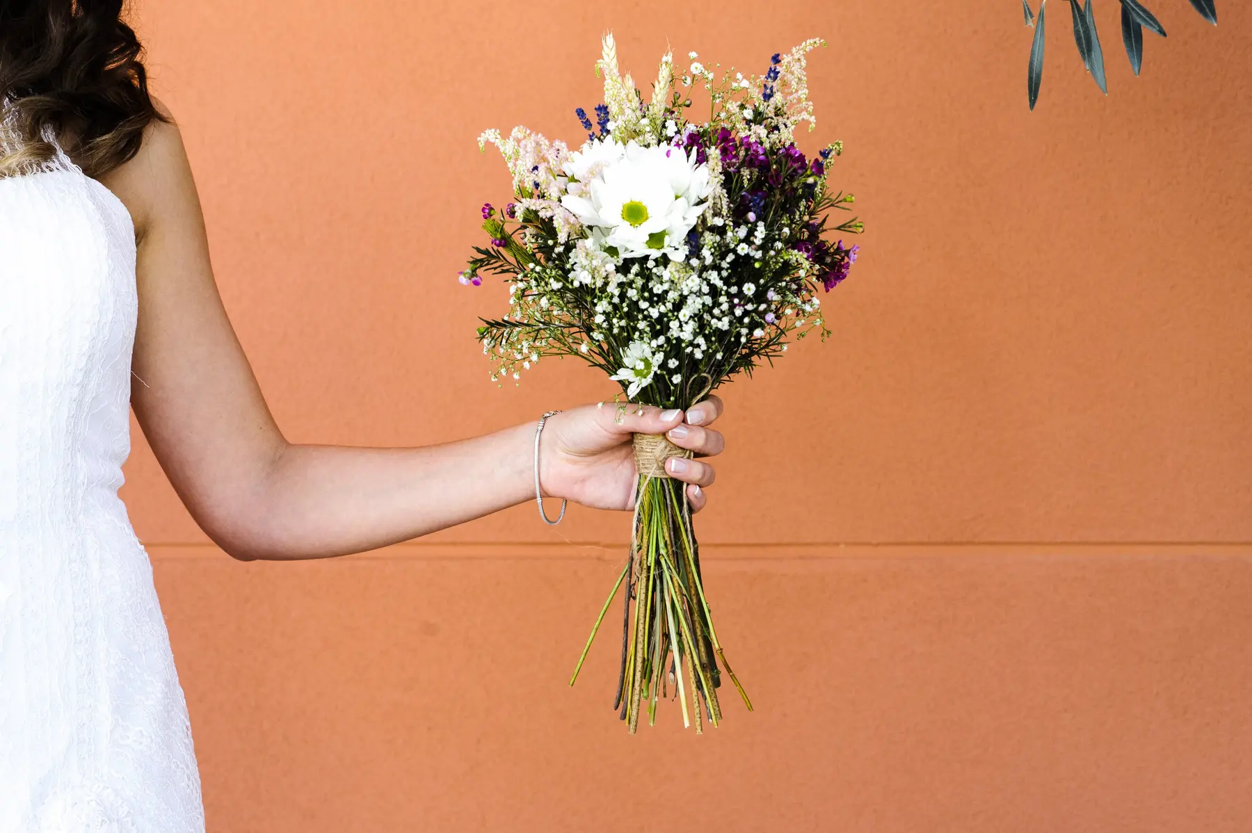 Detalle del ramo de una novia junto a una pared naranja