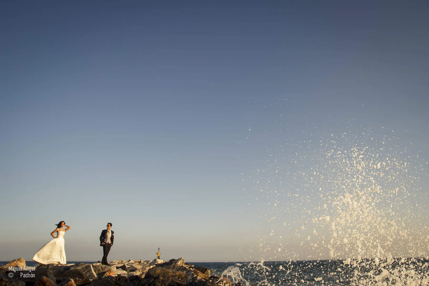 Novios junto al agua bajo un cielo azul