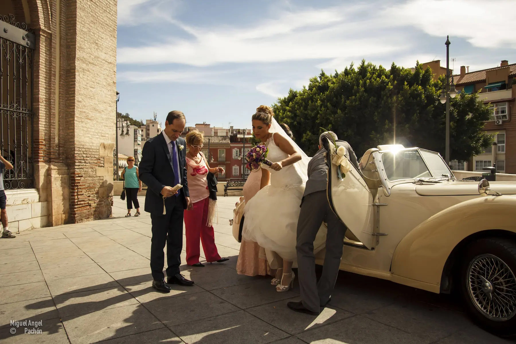 Novia junto a un coche acompañada por invitados