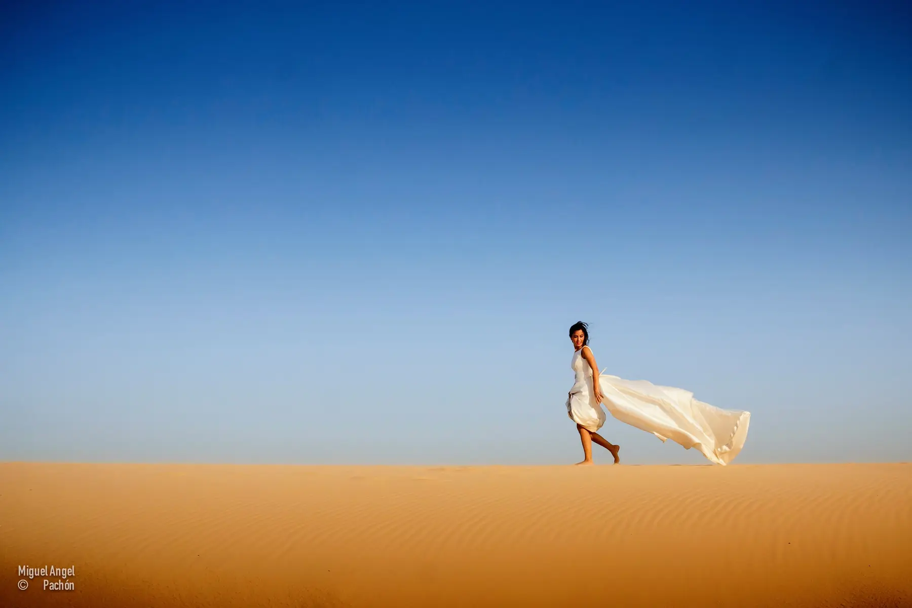 Novia caminando por una duna con el vestido al viento