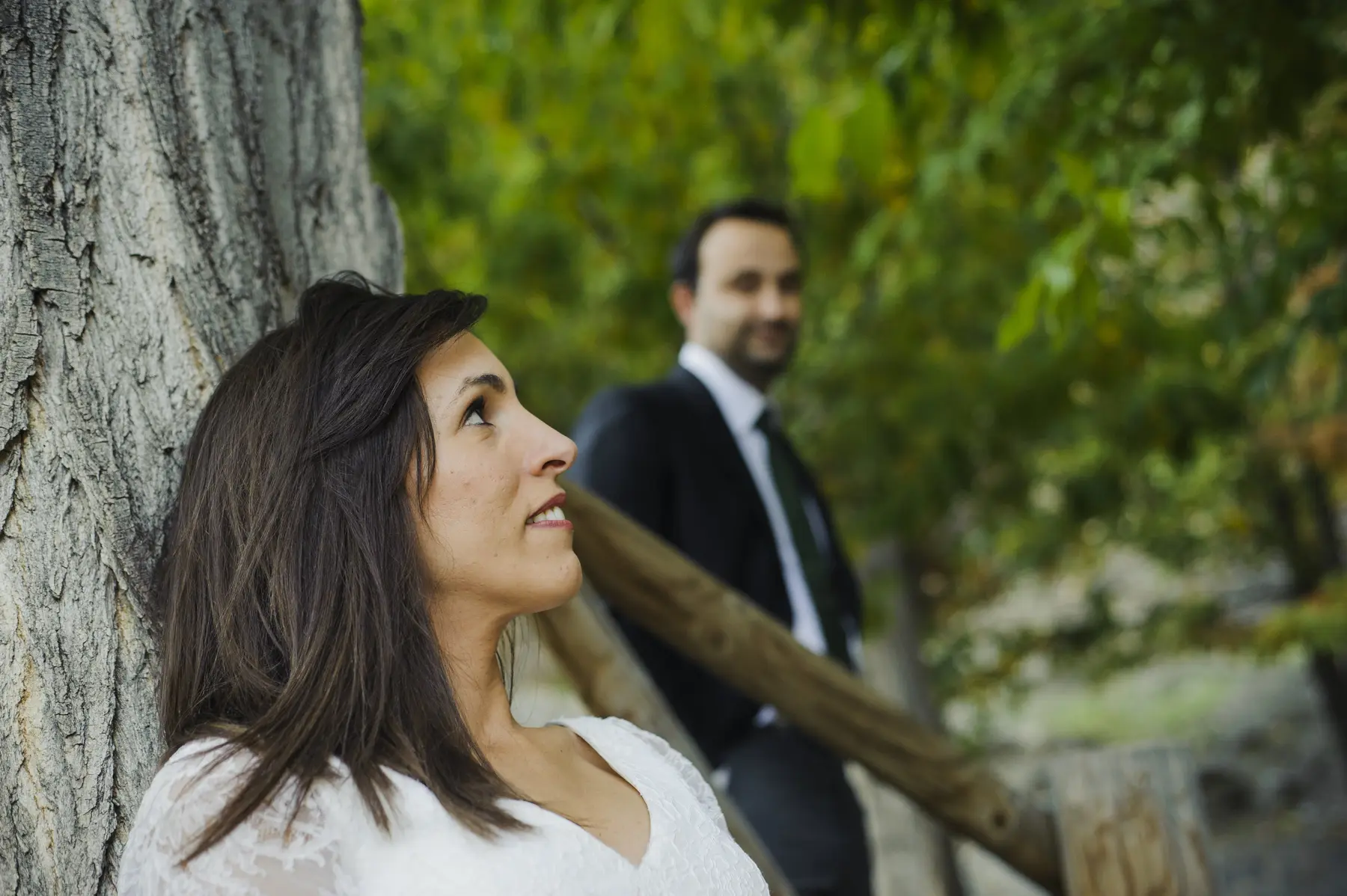 Novia en primer plano con el novio al fondo entre árboles