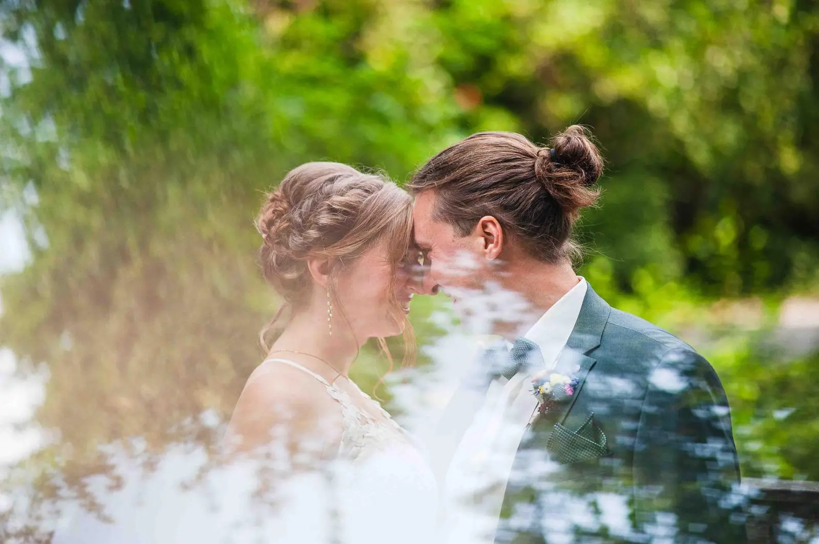 Beso de los novios entre reflejos y hojas