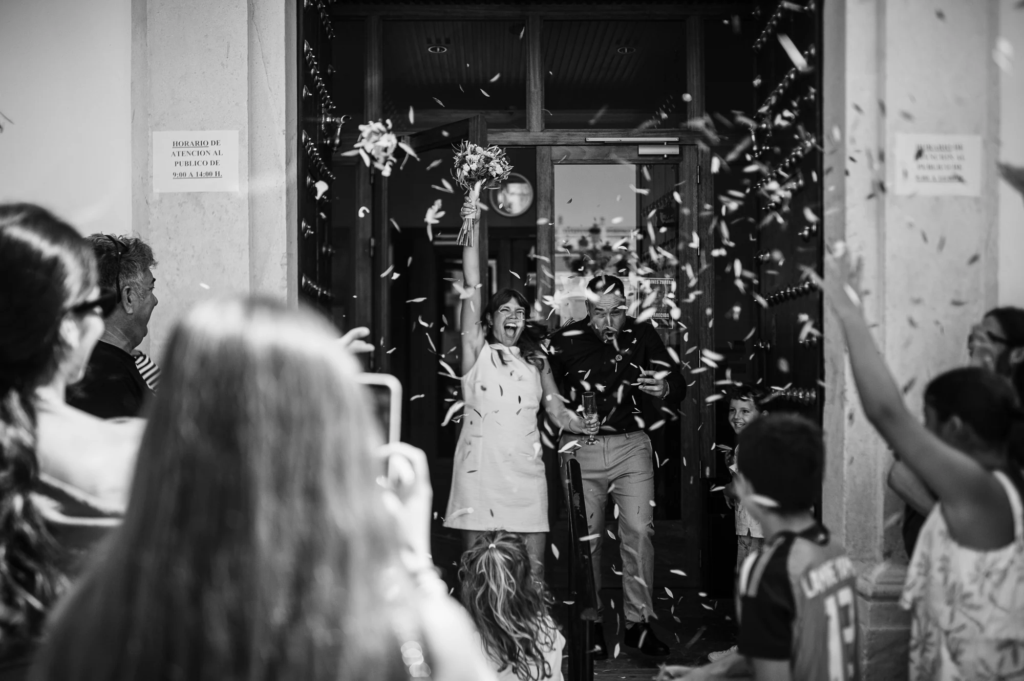 Invitados lanzando confeti a la salida de la boda en blanco y negro