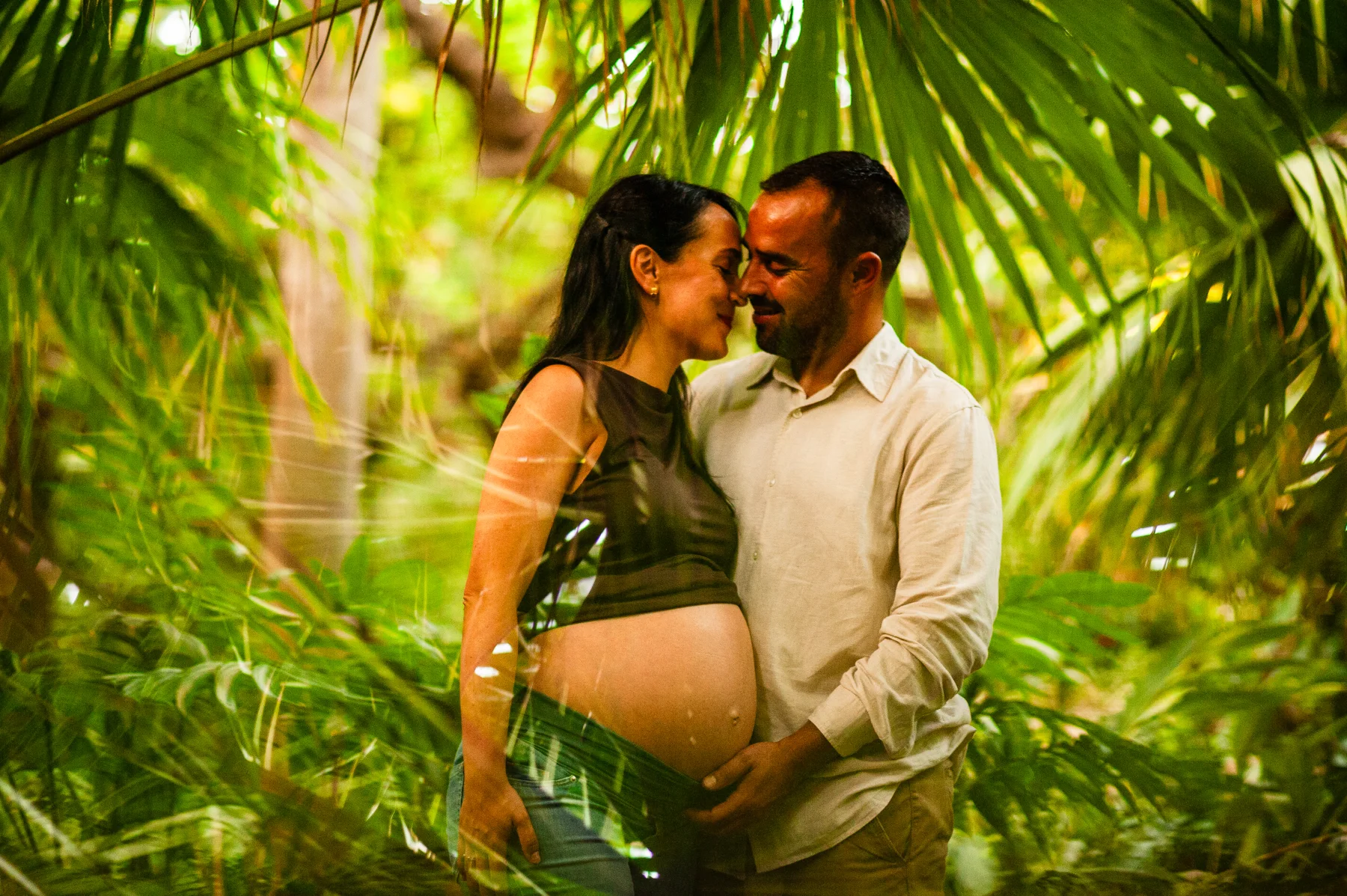 Beso de una pareja embarazada bajo palmeras