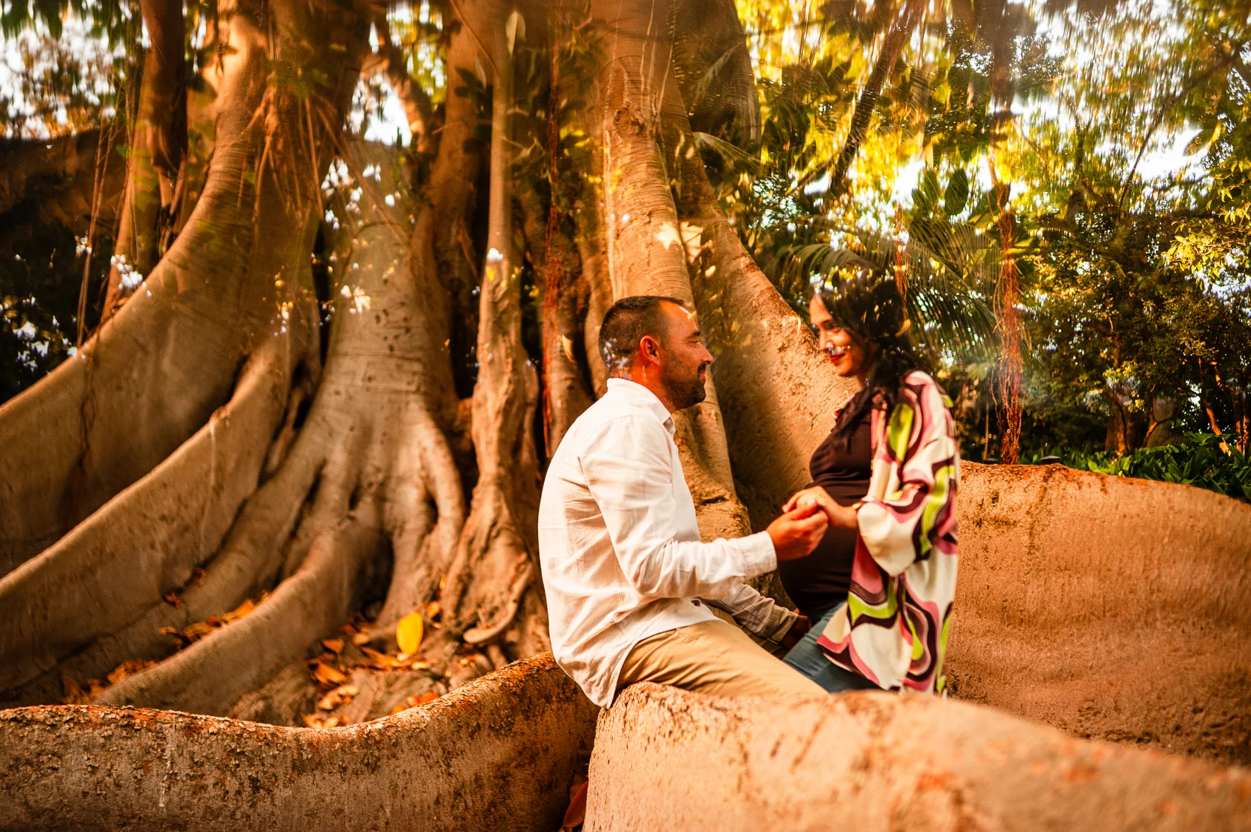 Pareja embarazada sentada junto a un árbol