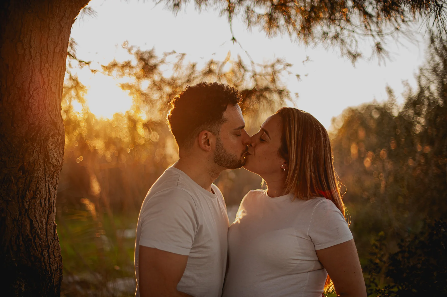 Beso de una pareja embarazada bajo un árbol