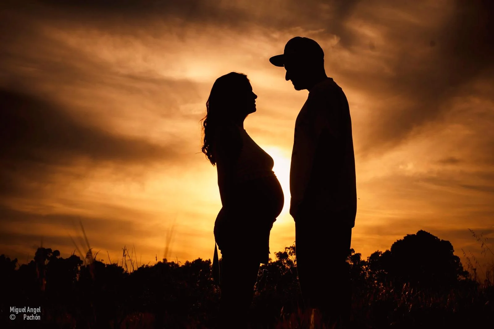 Siluetas de una pareja embarazada frente al cielo del atardecer