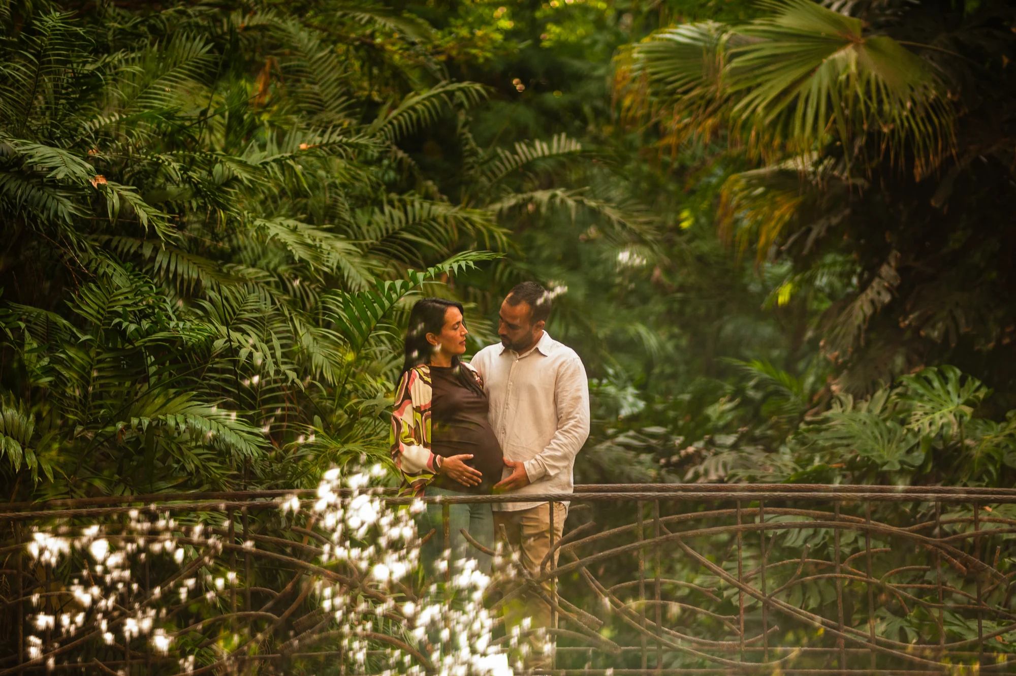 Pareja esperando un bebé, rodeada de vegetación en un jardín