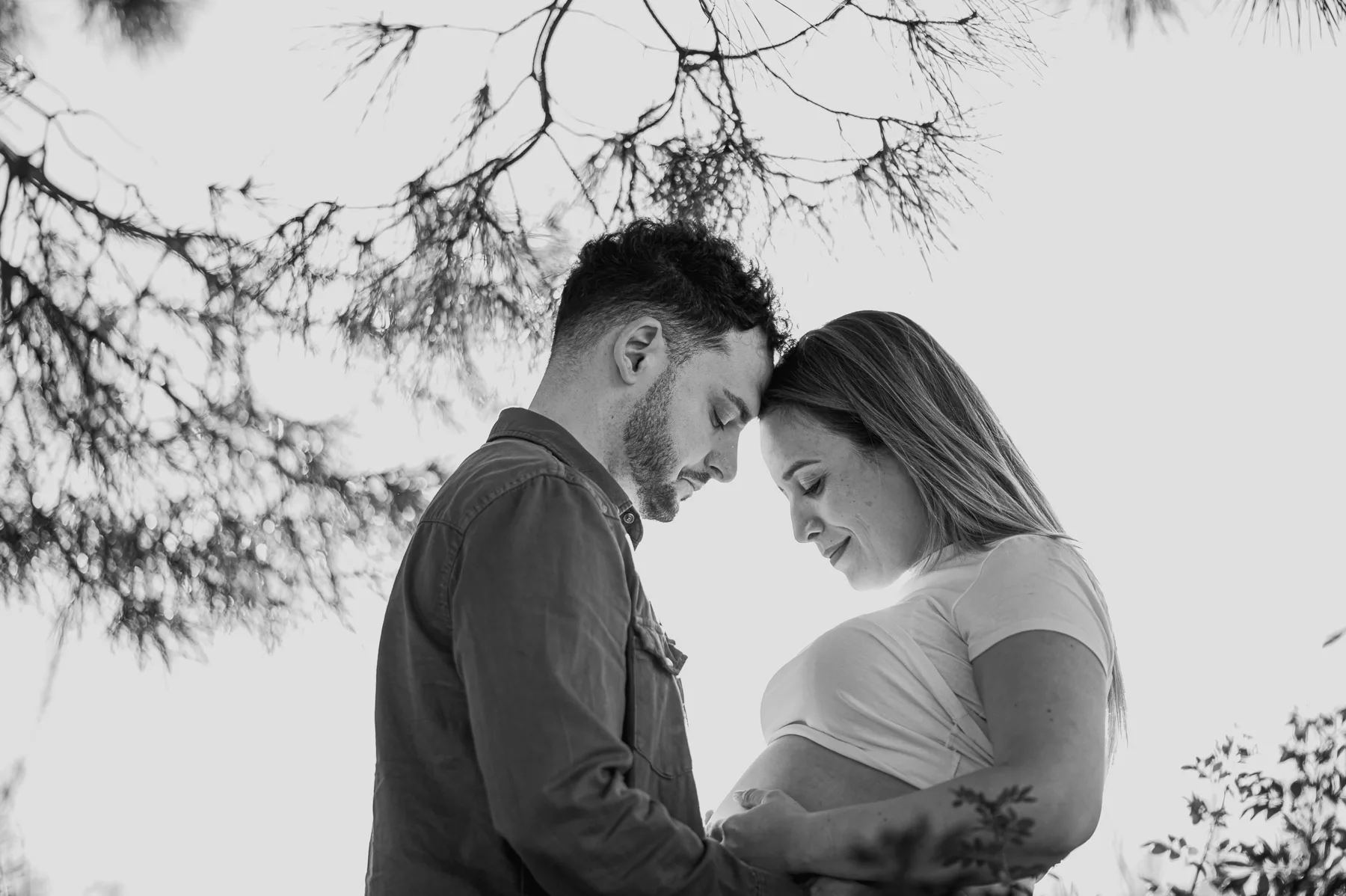 Pareja esperando un bebé bajo las ramas, en blanco y negro
